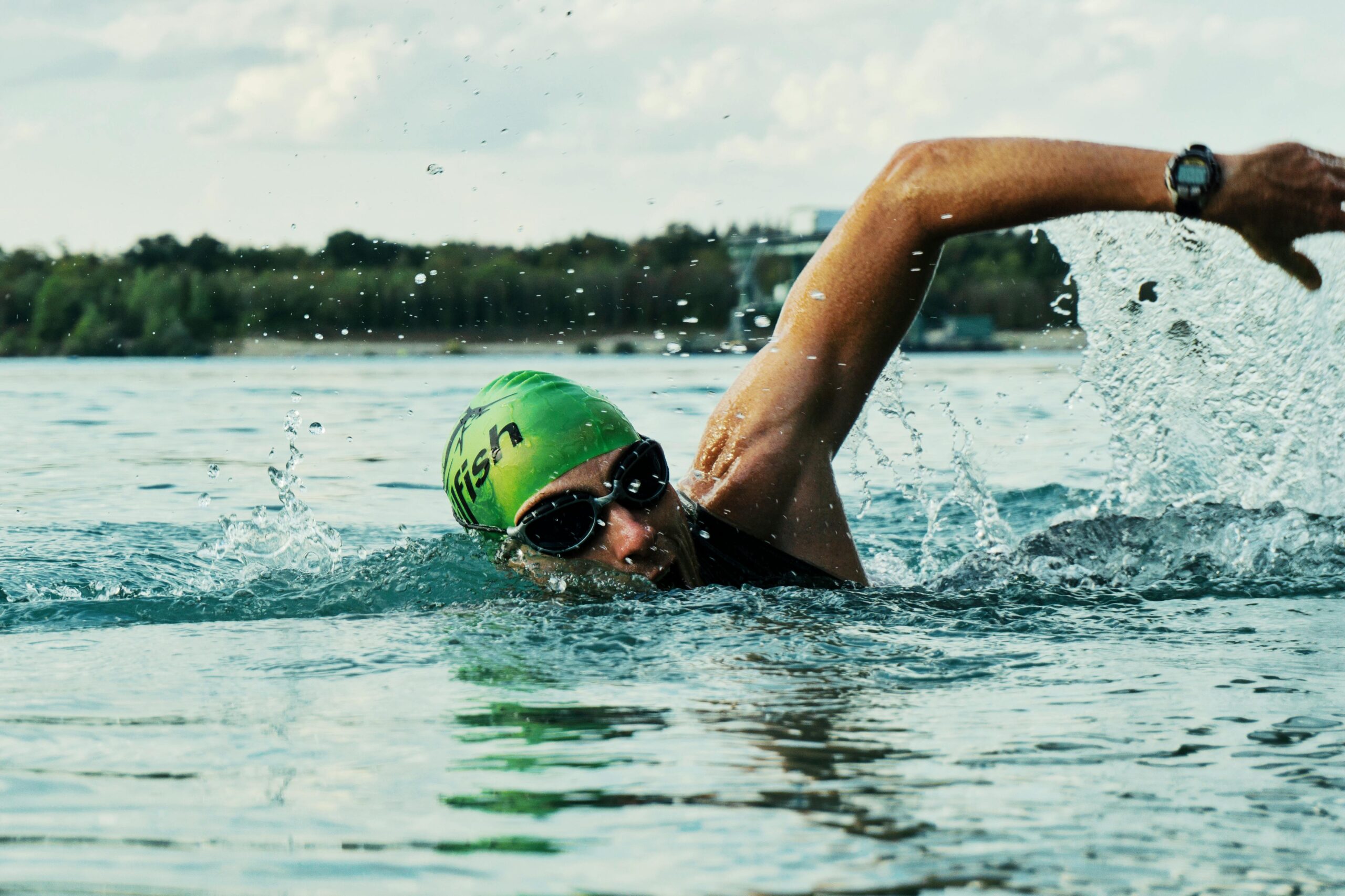Focused swimmer in open water wearing a green cap and goggles, symbolizing athletic performance and mental focus.
