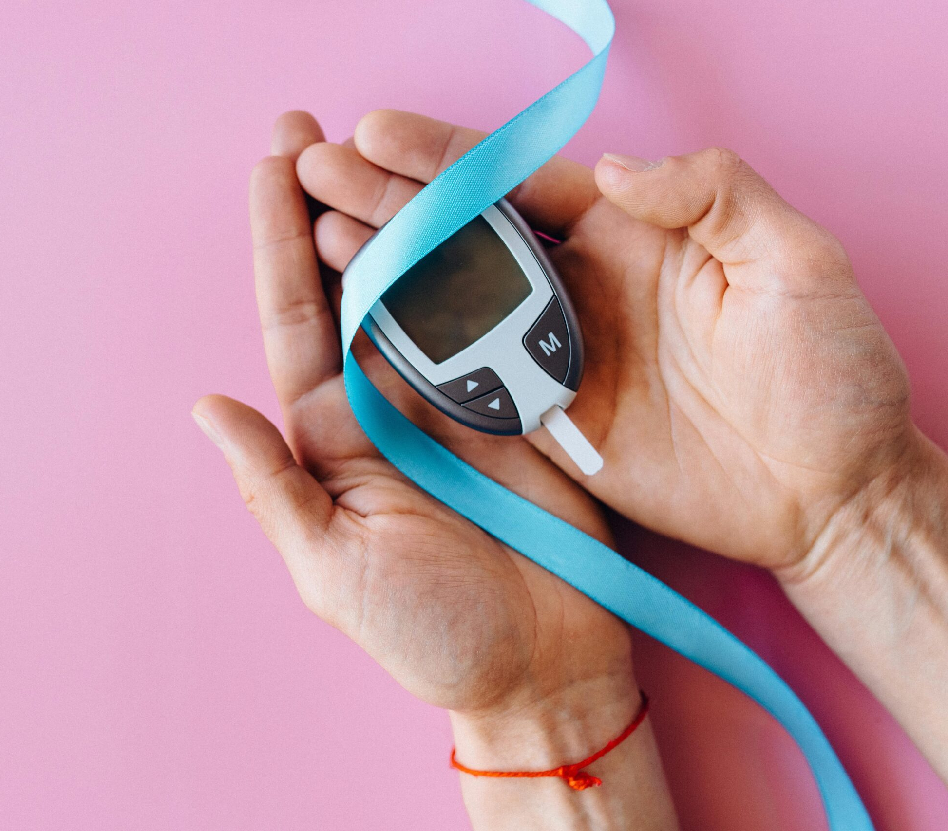 Hands holding a glucometer with a blue ribbon, symbolizing diabetes awareness and therapy for diabetics.