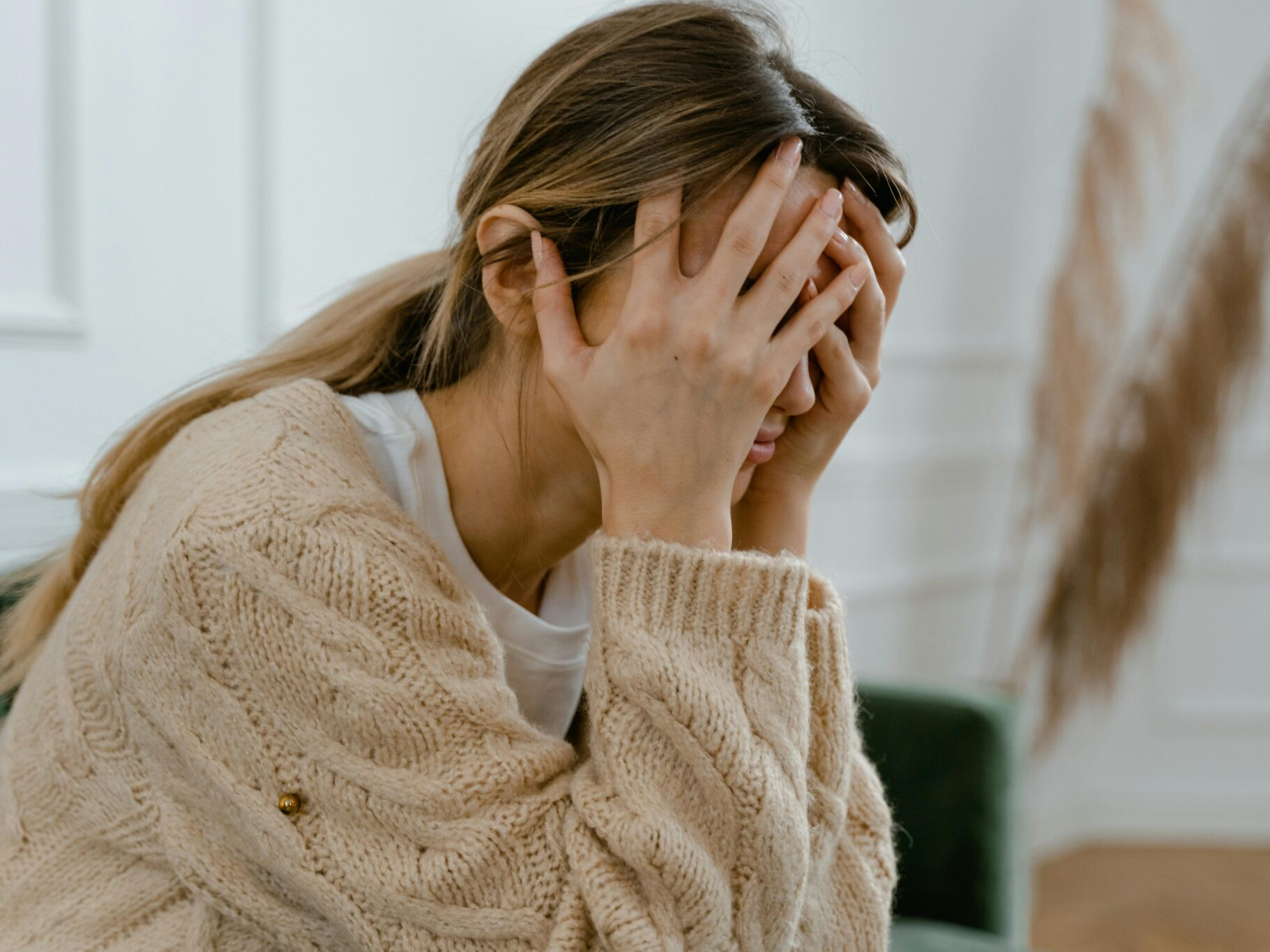 A woman sitting on a couch, overwhelmed and holding her face in her hands, showing signs of emotional exhaustion and distress.