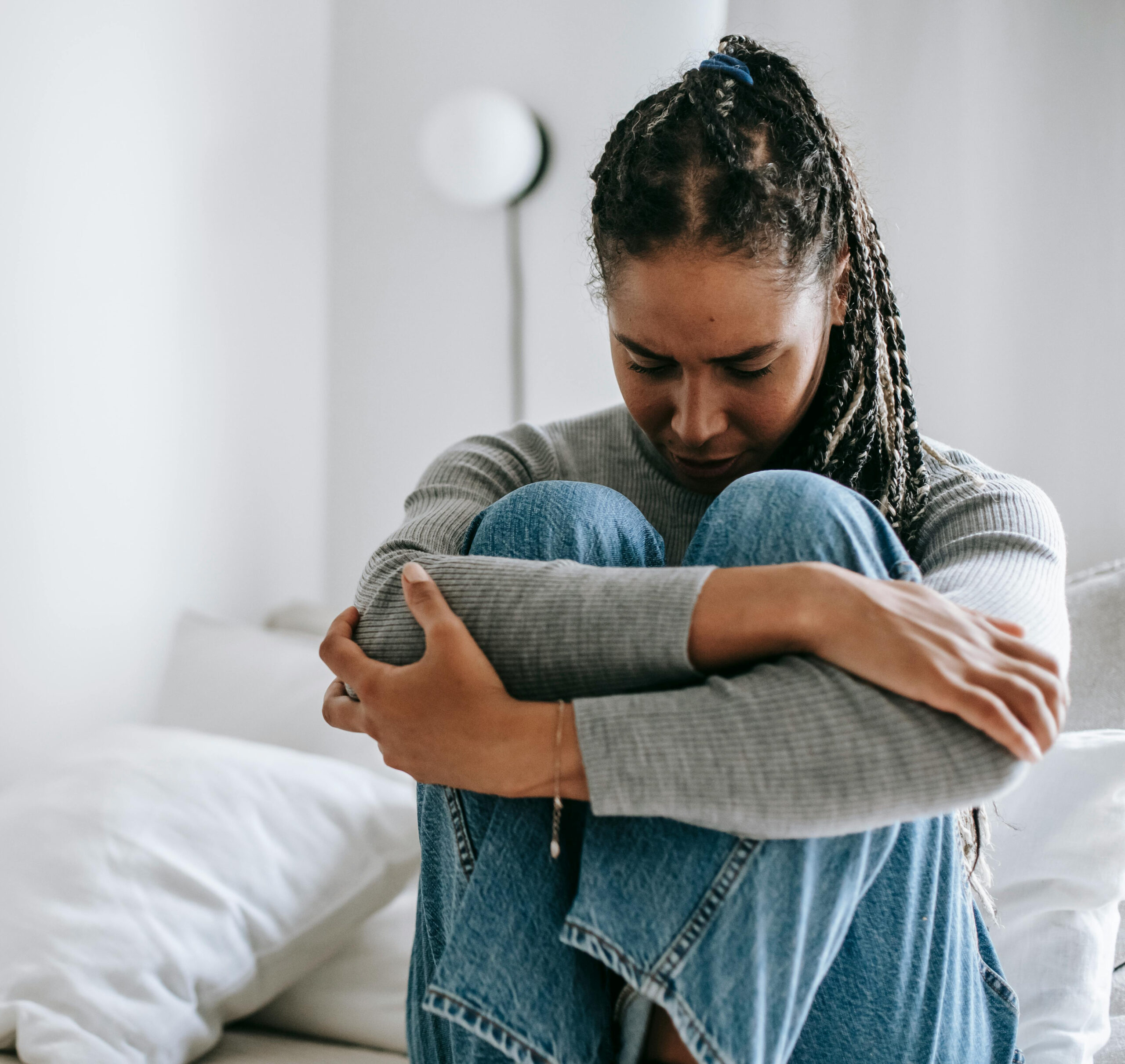 Upset ethnic woman embracing knees on bed