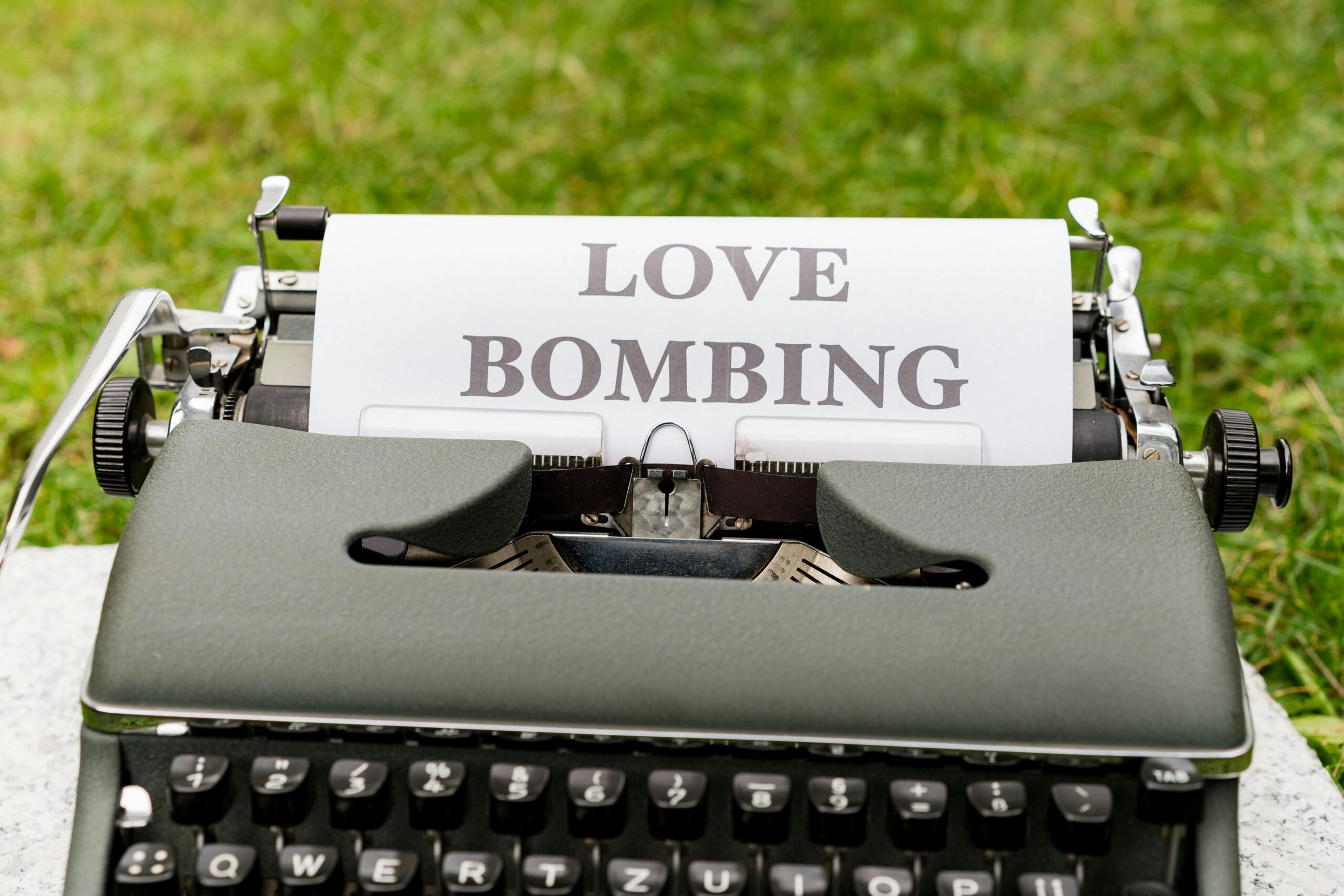 A close-up of a vintage typewriter with the words "LOVE BOMBING" typed on paper, symbolizing the early stage of narcissistic abuse.