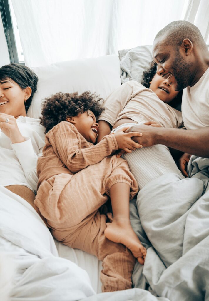 Happy multiracial family laughing and cuddling in bed, capturing moments of closeness and emotional connection in family life.