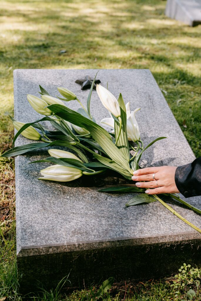Hand placing white flowers on a gravestone, symbolizing remembrance, mourning, and the experience of grief after losing a loved one.