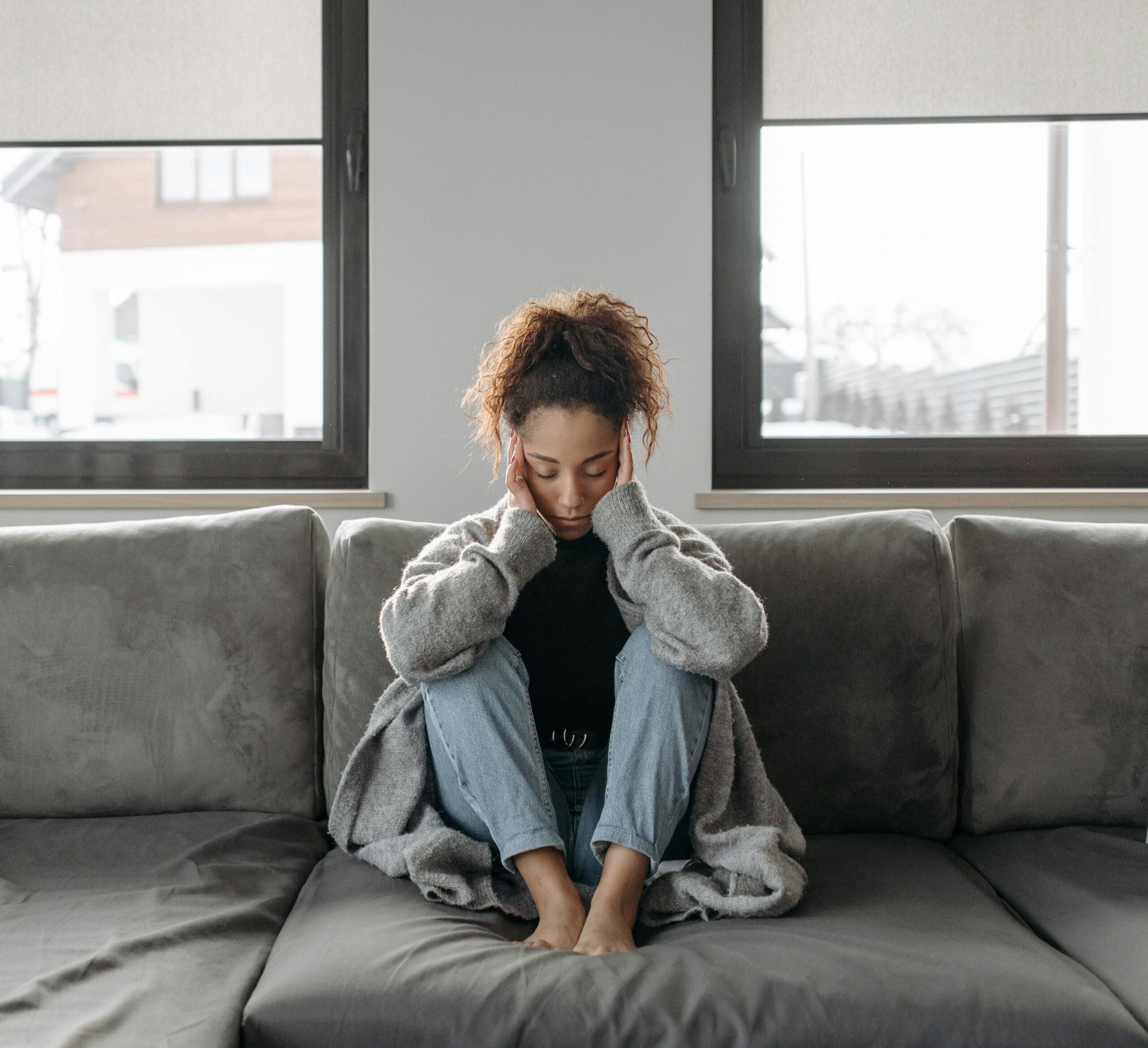 Person sitting quietly on a couch with hands on their face, reflecting feelings of isolation and overwhelm often associated with depression and emotional distress.