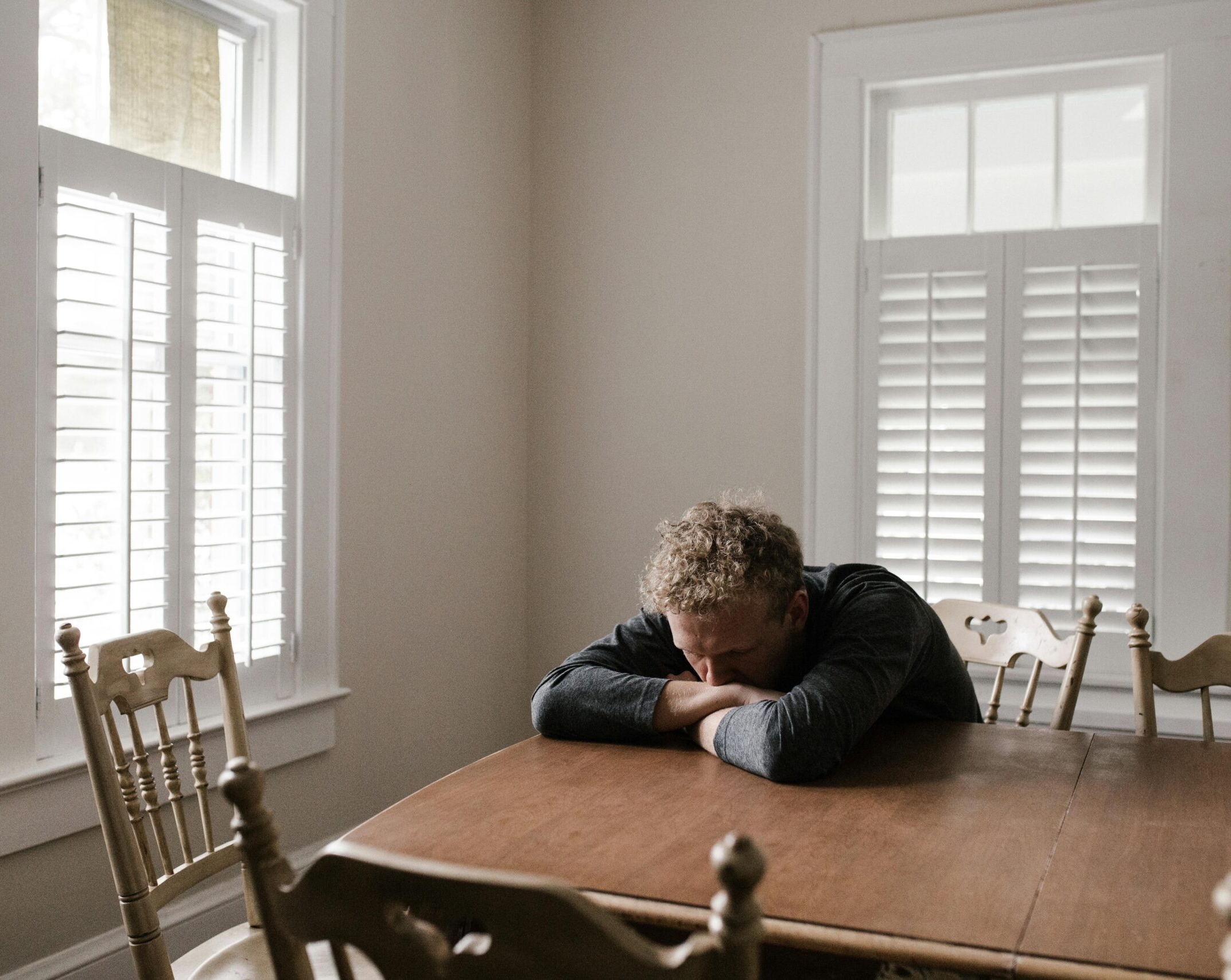 A man looking downcast with his head down on a table, representing an anxious man who needs therapy for anxiety.